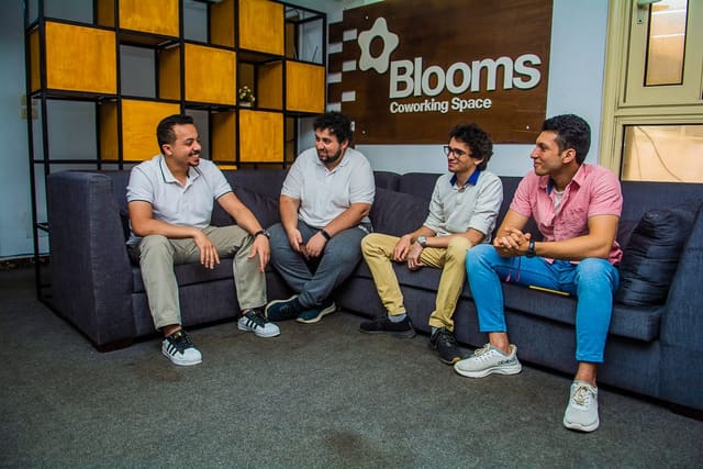 Four members talking on the lounge sofa beneath the Blooms Coworking Space sign