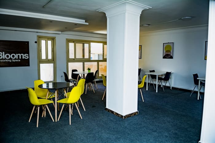 Open lounge floor at Blooms with yellow chairs and cafe tables near the Blooms sign