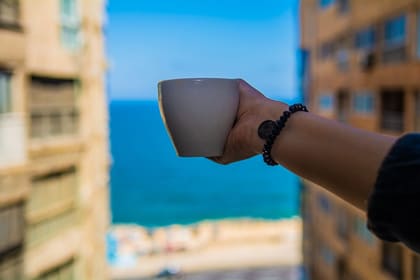 A member holding a coffee cup up to a window overlooking the Mediterranean in Roushdy, Alexandria